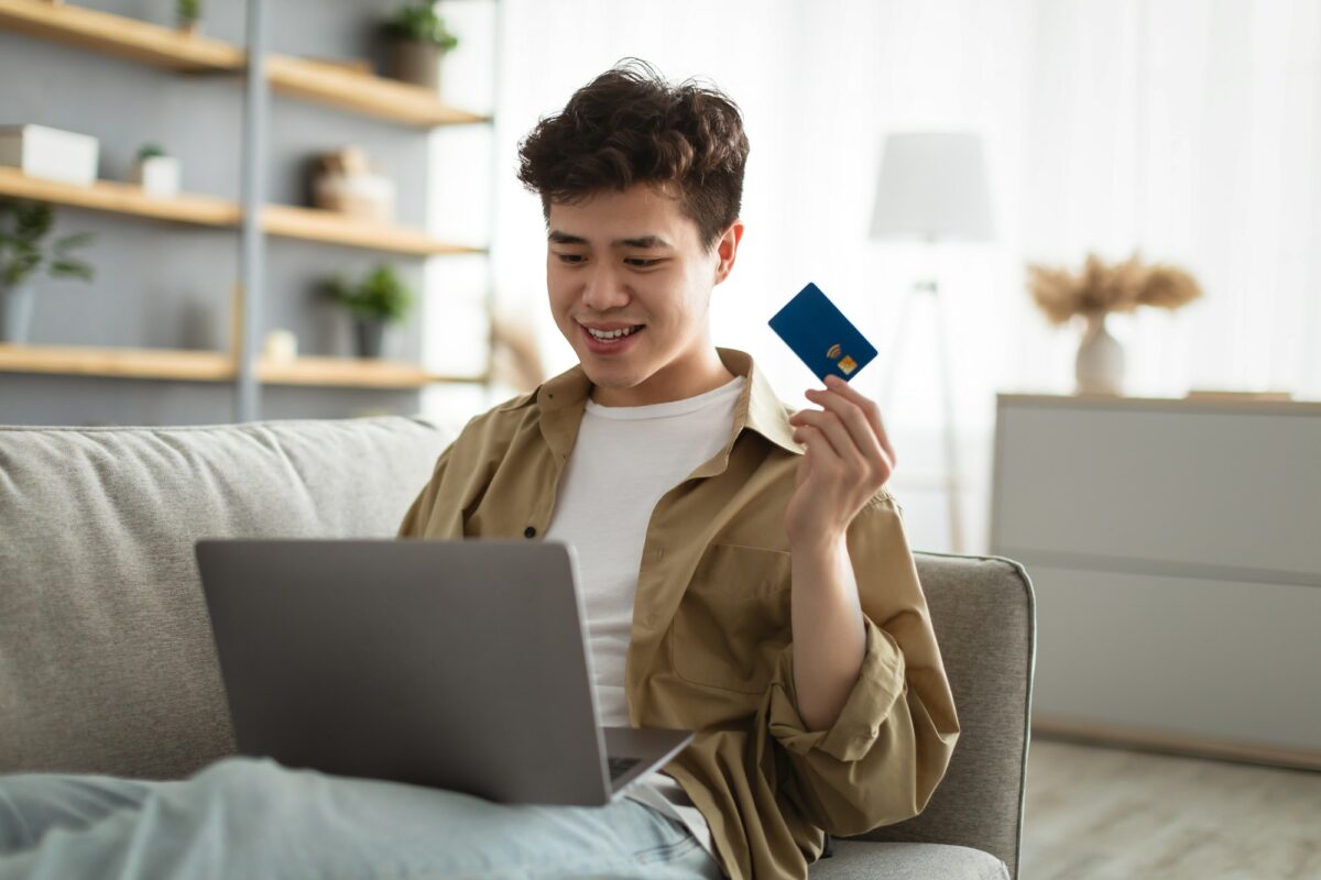 Smiling asian guy showing credit card at home