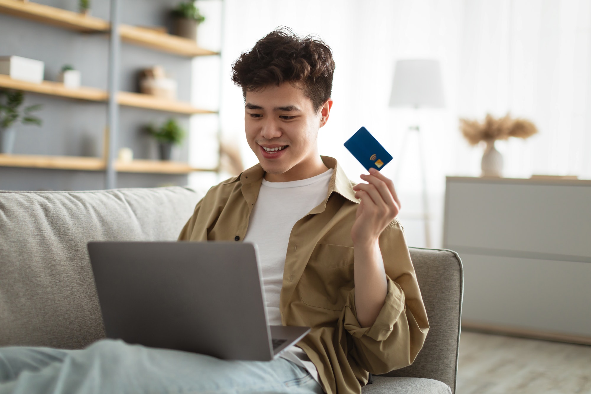 Smiling asian guy showing credit card at home